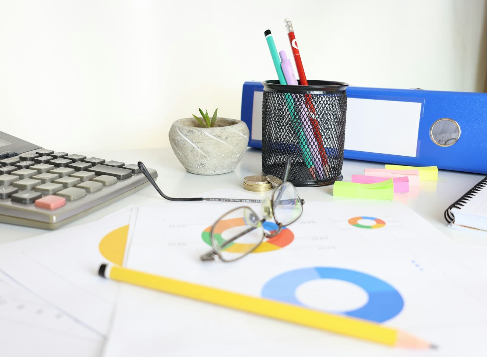 An office desk with files, charts, a calculator and reading glasses