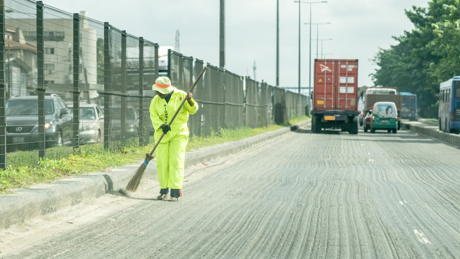 A sanitation worker in high-visibility overalls sweeping a road