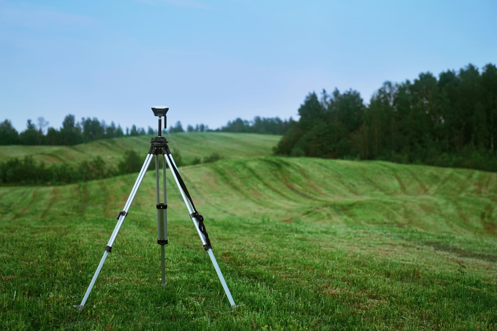 A surveyor's tripod standing in an open green field